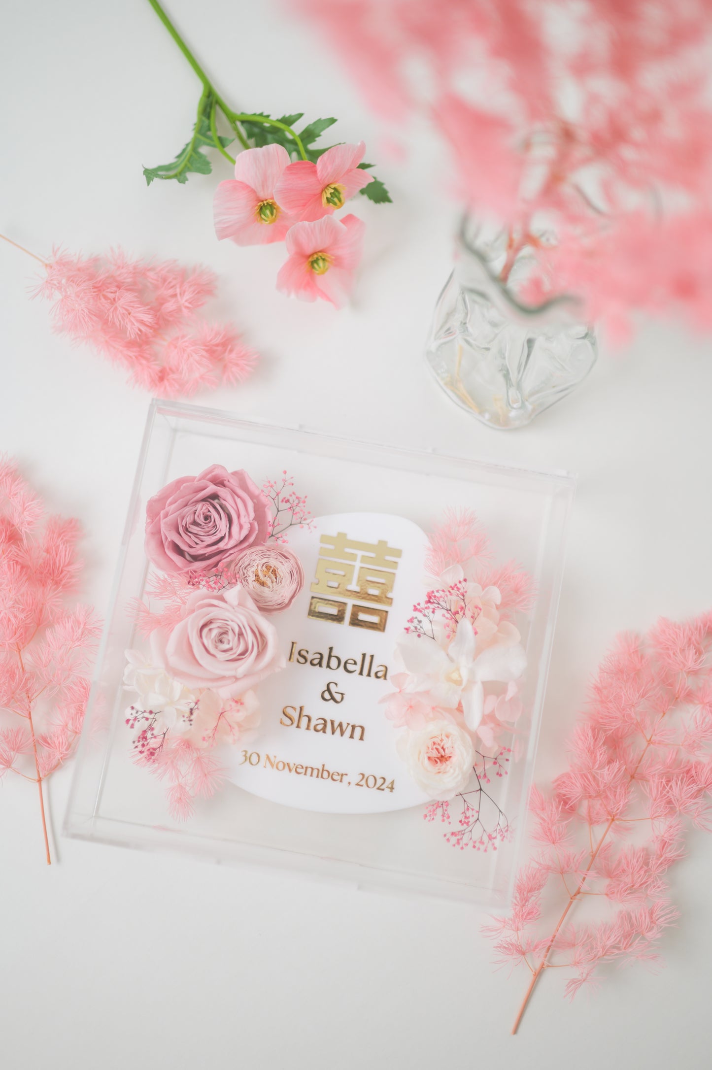 Personalized wedding frame with preserved pink flowers, featuring custom names Isabella & Shawn and a wedding date, with elegant floral design in a clear acrylic display.