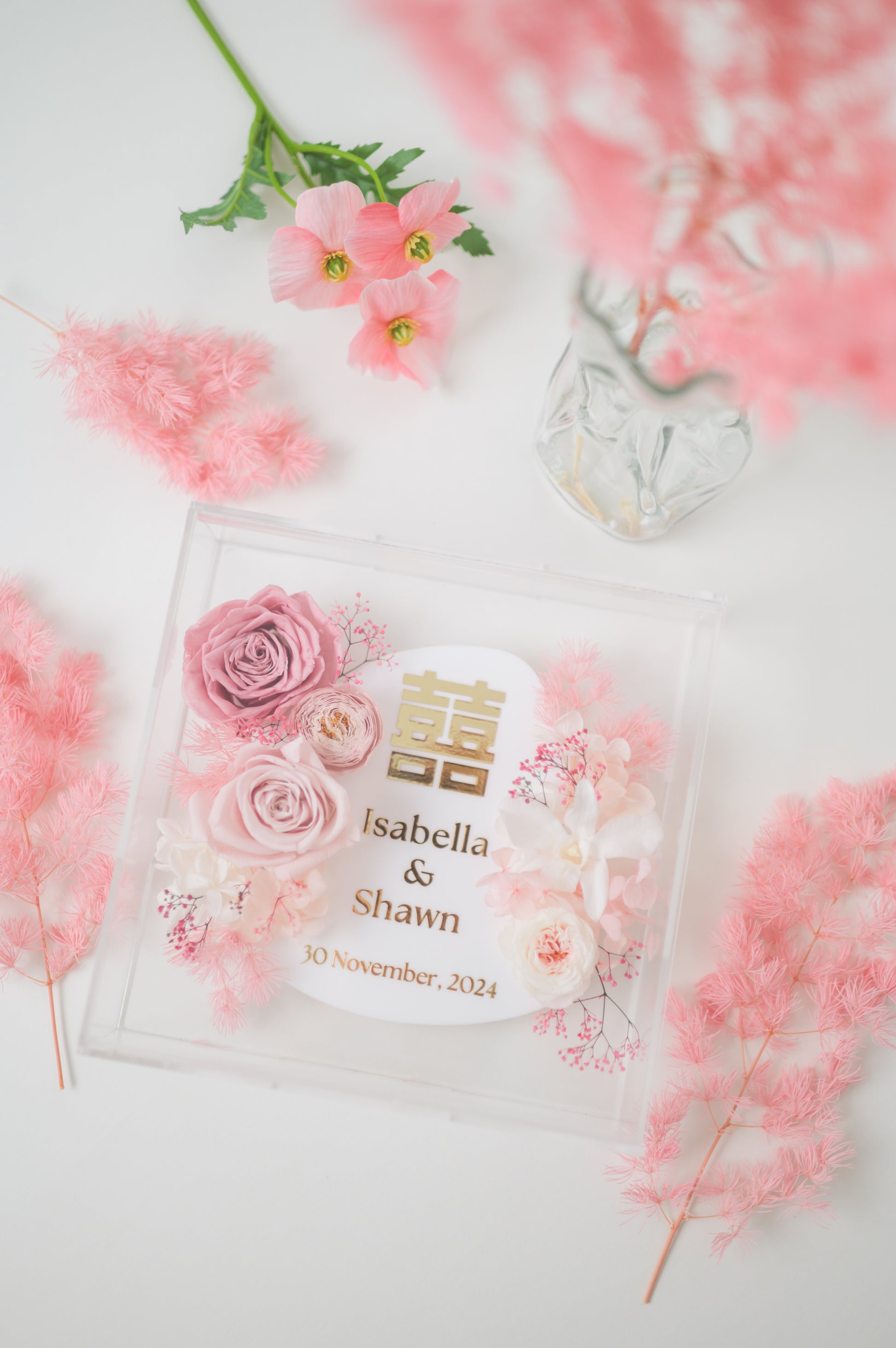 Personalized wedding frame with preserved pink flowers, featuring custom names Isabella & Shawn and a wedding date, with elegant floral design in a clear acrylic display.