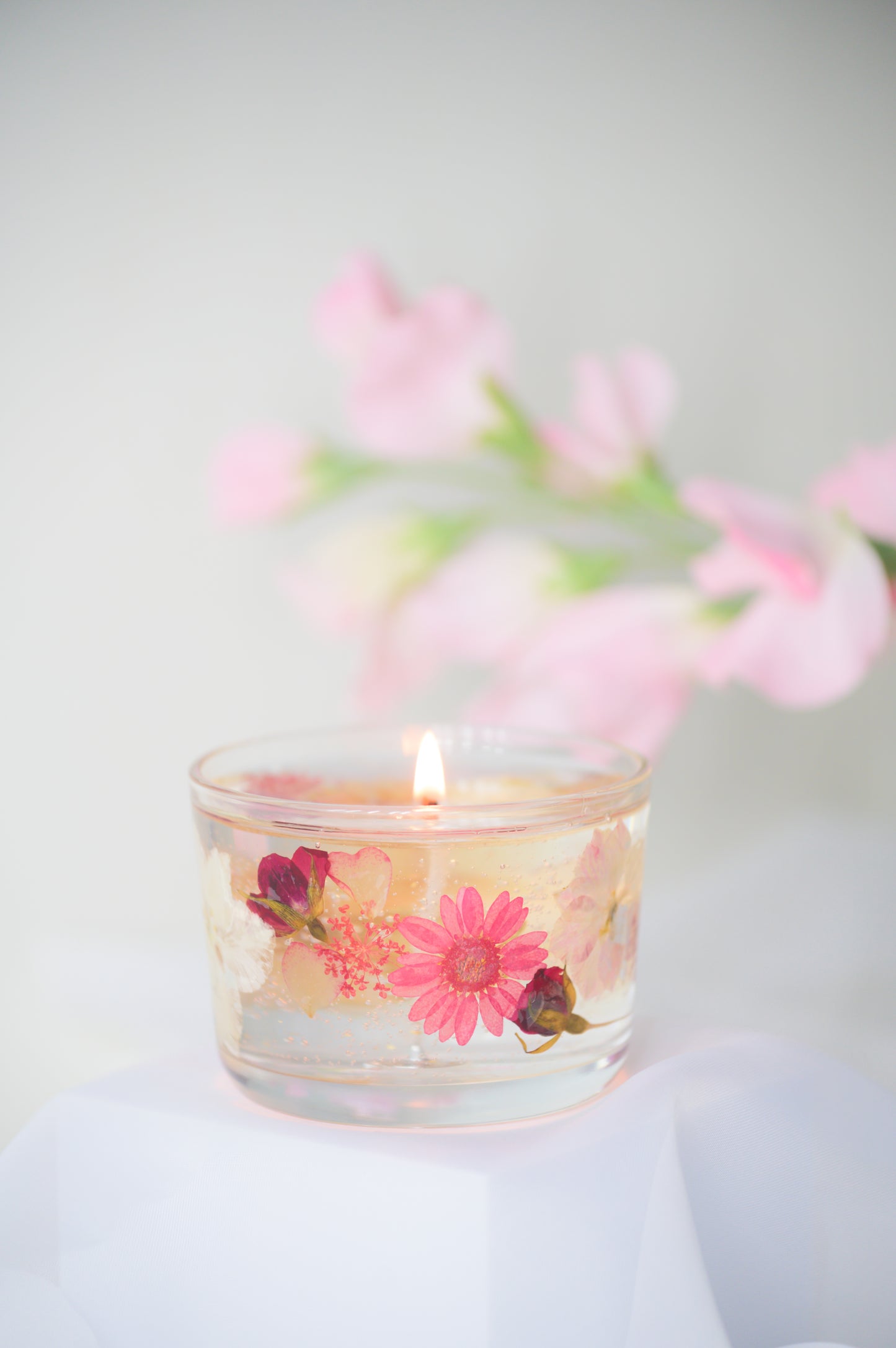 A beautiful gel candle embedded with dried pink flowers, including daisies and roses, delicately burning with soft light, creating a romantic and elegant ambiance.