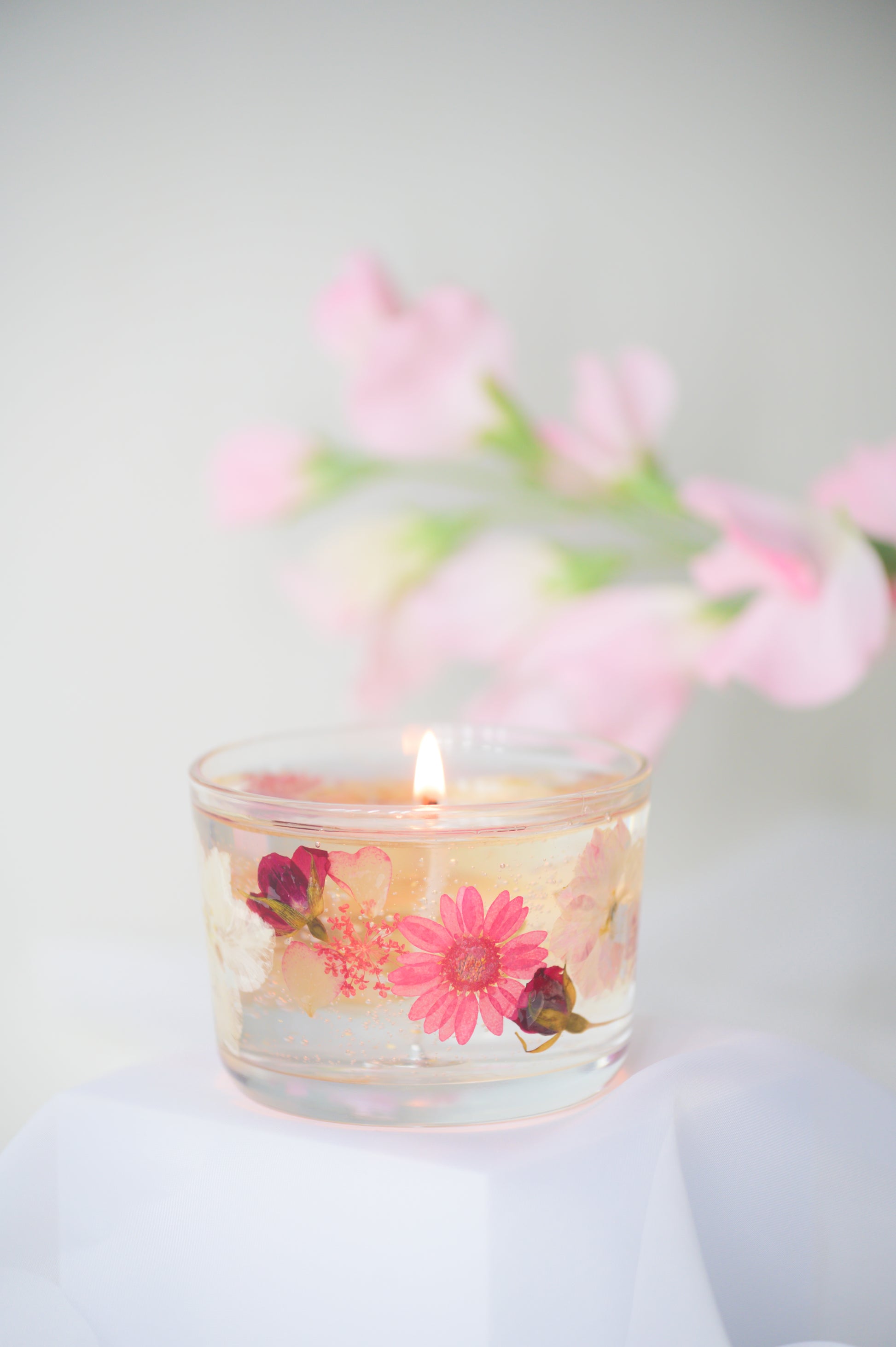 A beautiful gel candle embedded with dried pink flowers, including daisies and roses, delicately burning with soft light, creating a romantic and elegant ambiance.